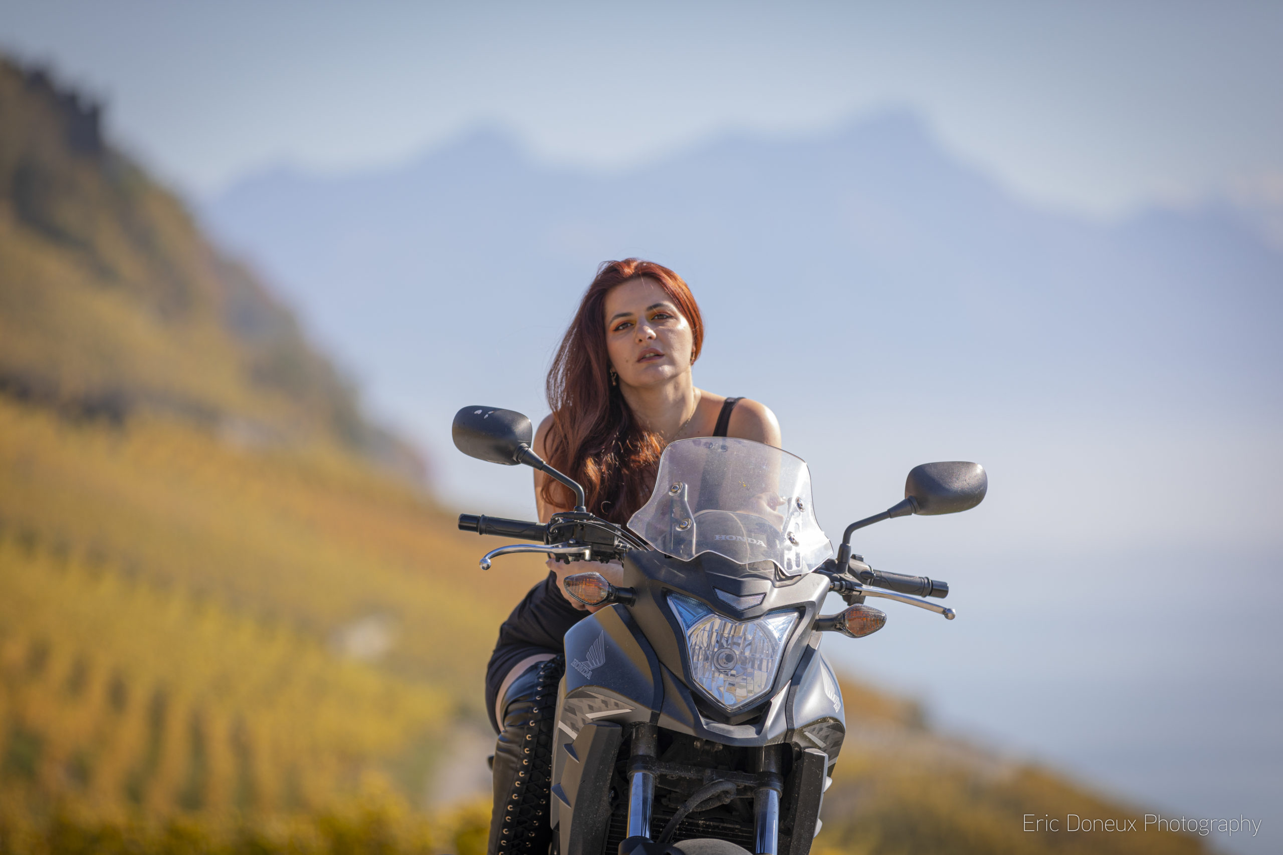 Jeune femme en robe courte et grandes bottes sur sa moto dans le Lavaux