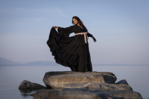 Jeune femme en robe noire sur un rocher au bord d'un lac